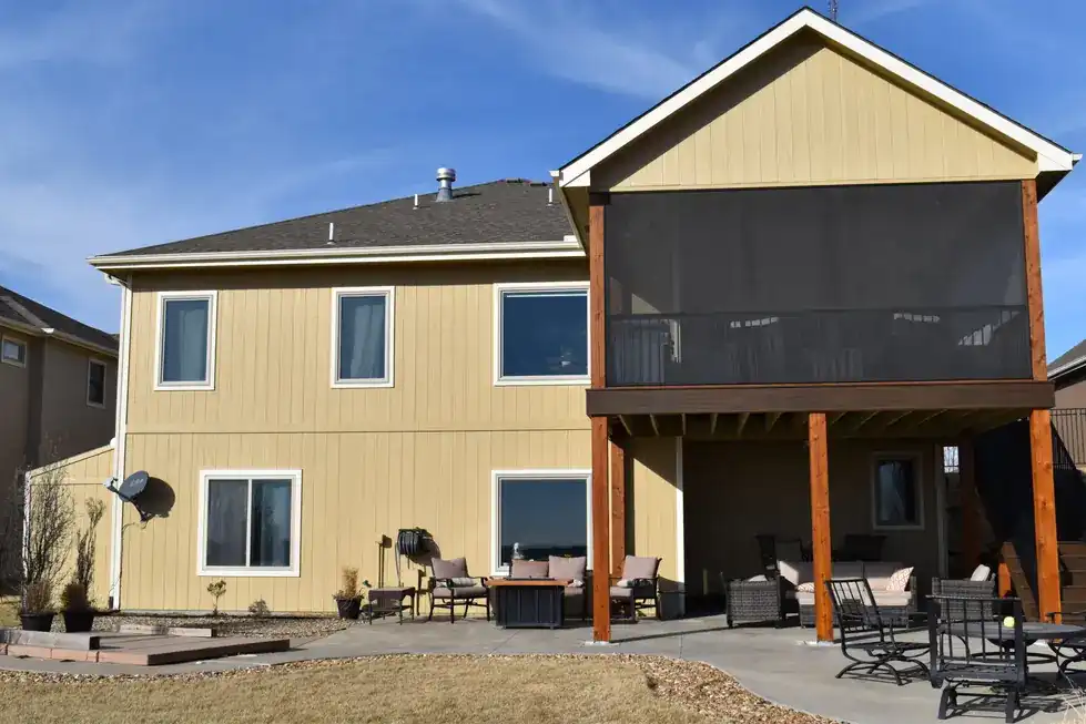 Rear of a yellow-sided home with a PDQ screened porch addition over a stone patio