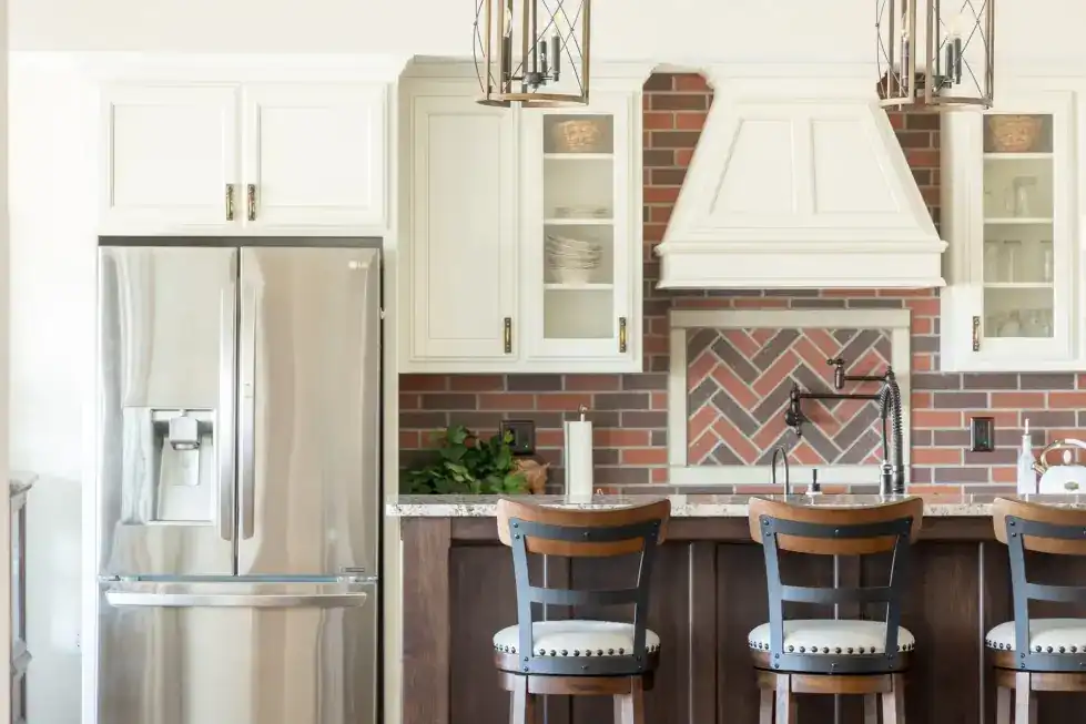 A finished PDQ kitchen: herringbone brick backsplash under a painted range hood, walnut island and three counter stools